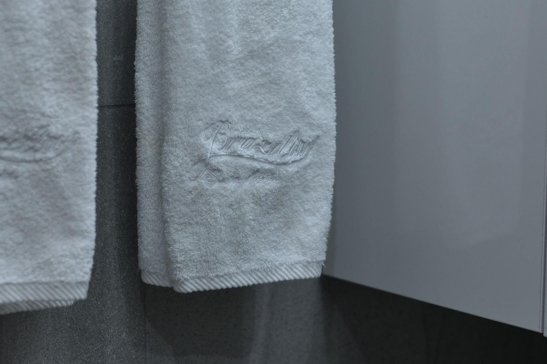 A close-up of a grey towel with embossed text, hanging on a dark surface.