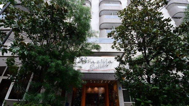 The entrance to a hotel named 'Brazilia Suites' with a modern design, surrounded by lush greenery. - Brazilia Suites Hotel (Baabda)