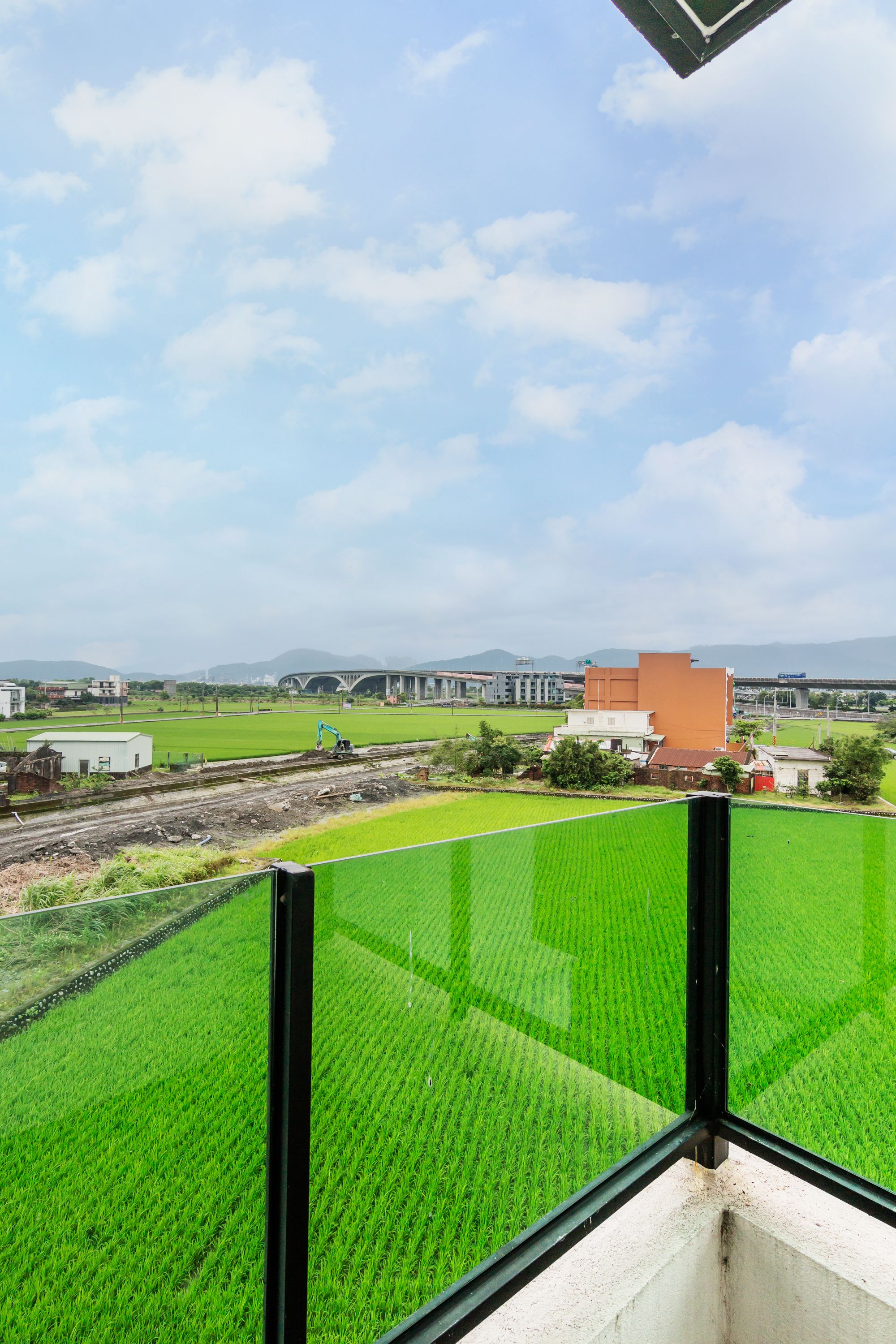 A view from a balcony with a green field, a bridge, and buildings in the background.