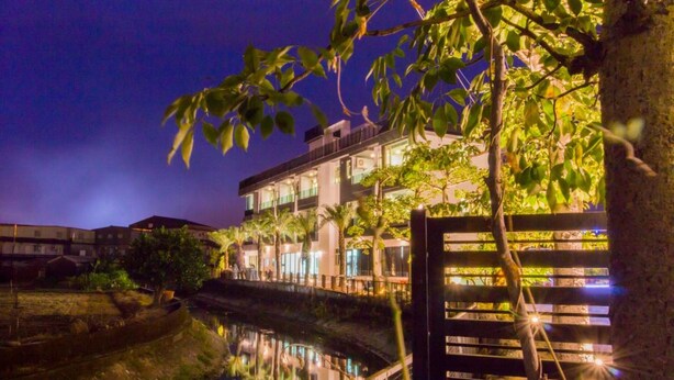 A multi-story hotel with a reflective water body in front, surrounded by trees and illuminated by ambient lighting. - Kano Resort (Luodong)