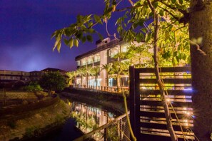A multi-story hotel with a reflective water body in front, surrounded by trees and illuminated by ambient lighting. - Kano Resort (Luodong)
