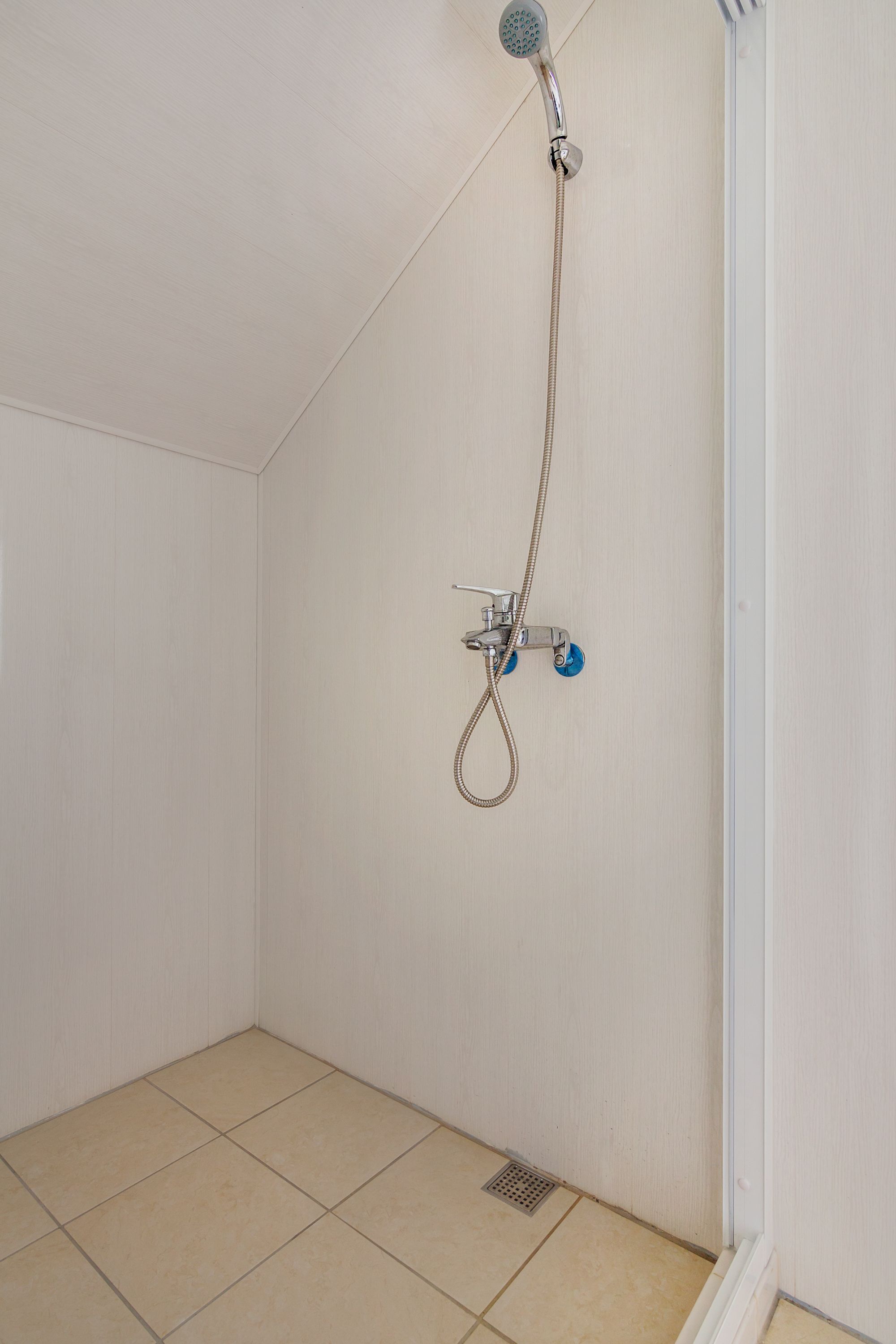 A small, tiled shower room with a handheld showerhead and a wall-mounted faucet.