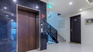 A modern lobby with a marble wall, a wooden elevator, a staircase, and a black door. - Kano Resort (Luodong)