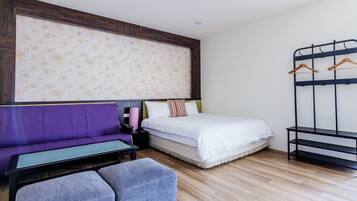 Una habitación con una cama, un sofá morado, una mesita y un banco.