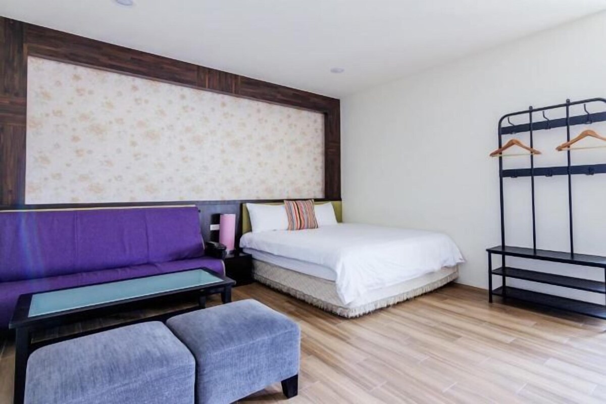 A bedroom with a bed, a purple sofa, a small table, and a bench.