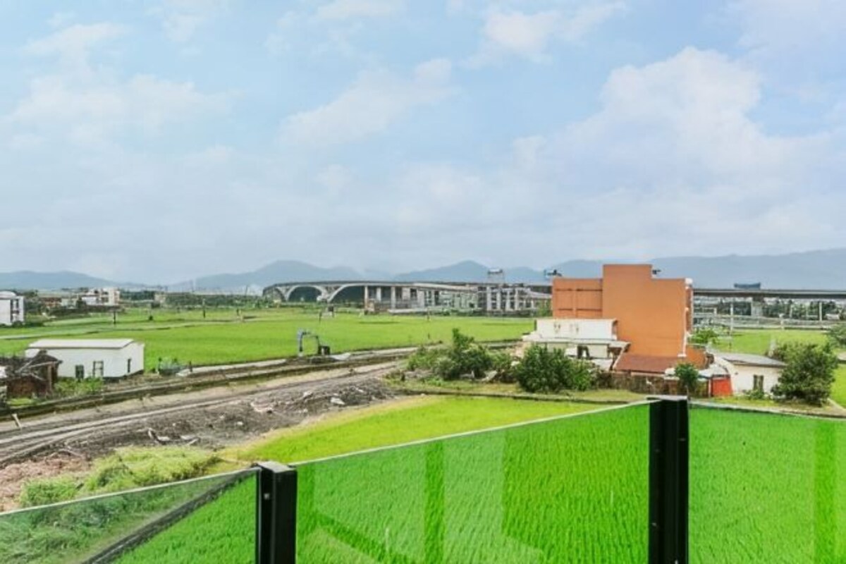 A view of green fields, a railway track, and a building with a red roof.
