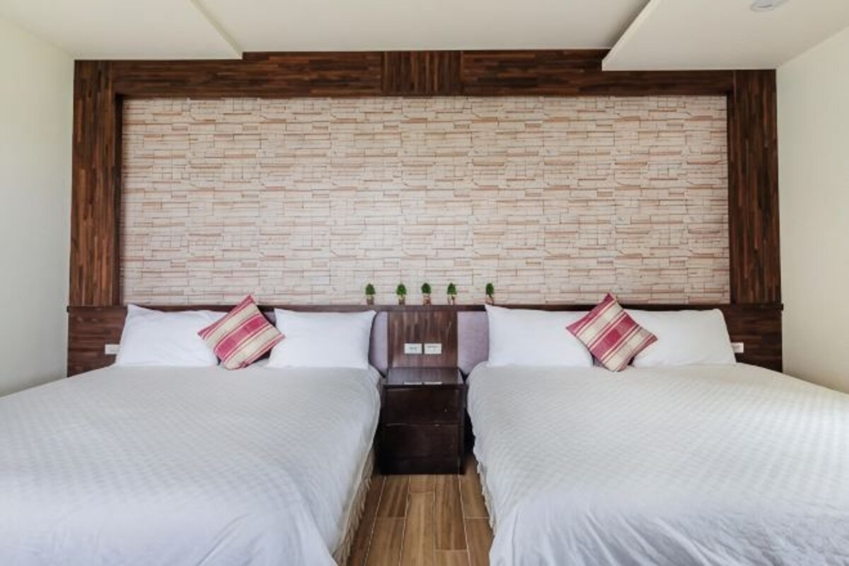 A double room with two beds, a brick-patterned headboard, and a small table between the beds.