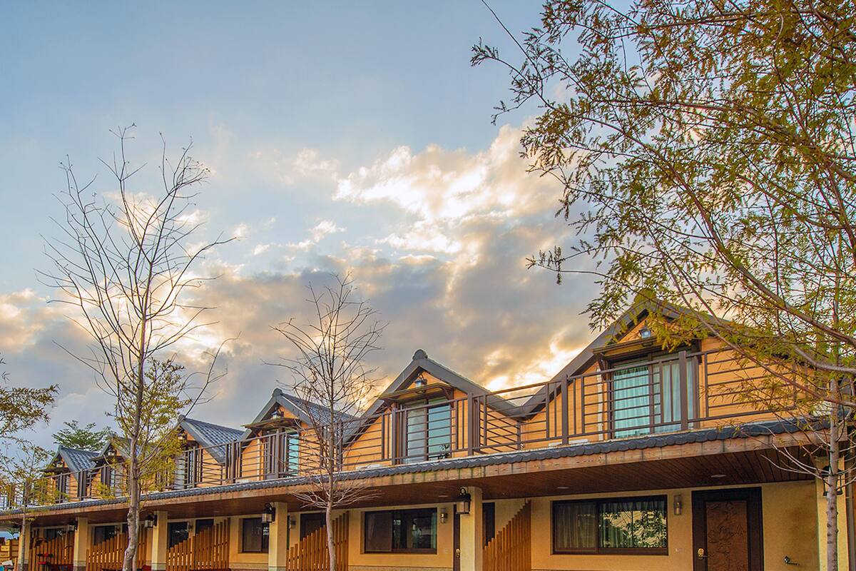 A row of wooden cabins with balconies, a paved courtyard, and a clear sky.