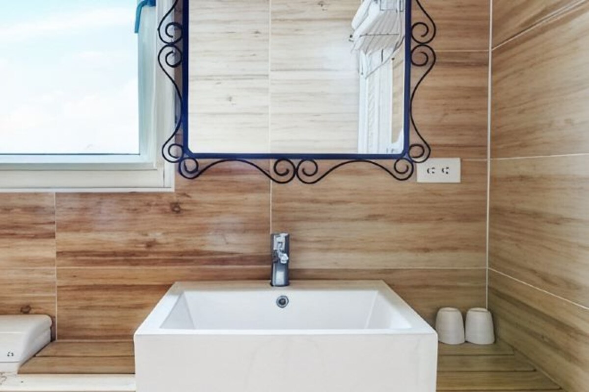 Une salle de bain avec un lavabo blanc, un miroir doté d’un cadre décoratif et des carreaux de mur en bois.