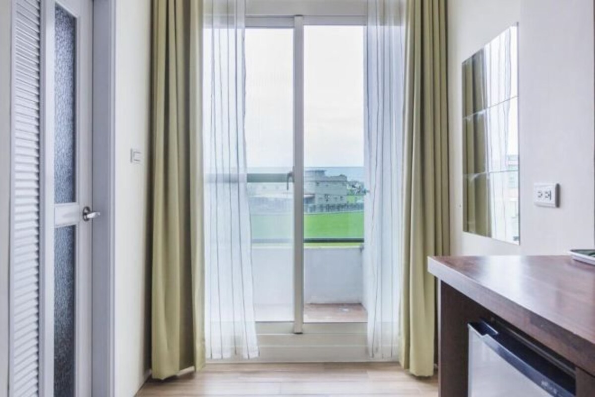 A room with a sliding glass door leading to a balcony, a wooden counter, and a wall-mounted mirror.