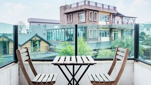 A balcony with two wooden chairs and a table, overlooking a building with a glass facade and a rooftop garden. - Kano Resort (Luodong)