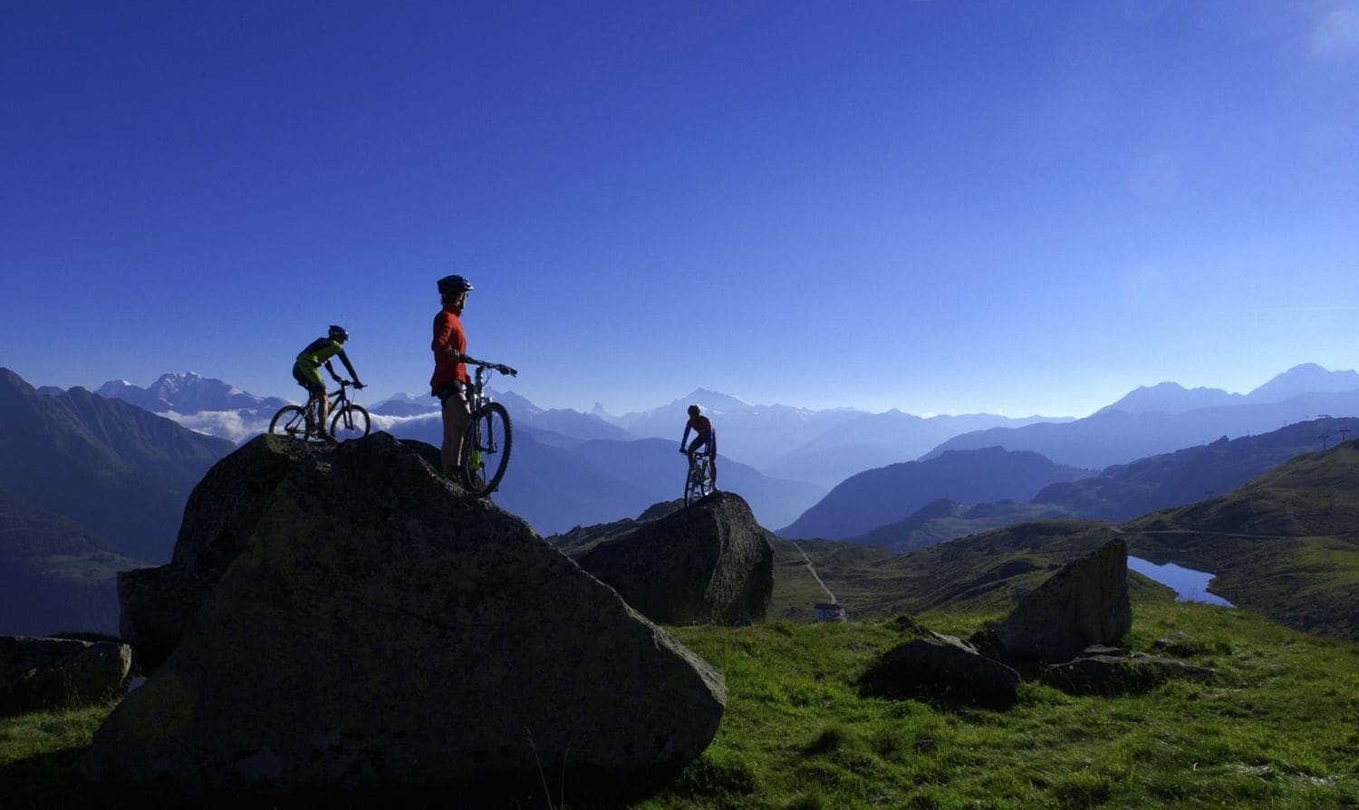 Three cyclists on large rocks with a mountainous landscape in the background.