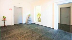 A hallway with dark tiled flooring, white walls, and doors. There are potted plants on a small table and a stack of stones. - Gästehaus St. Ursula (Brig)