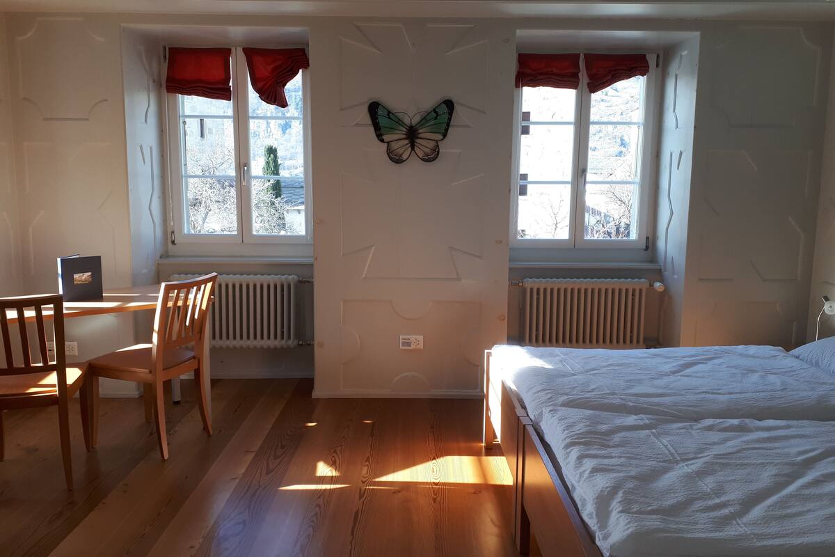 A room with a bed, a desk, and two windows with red curtains.