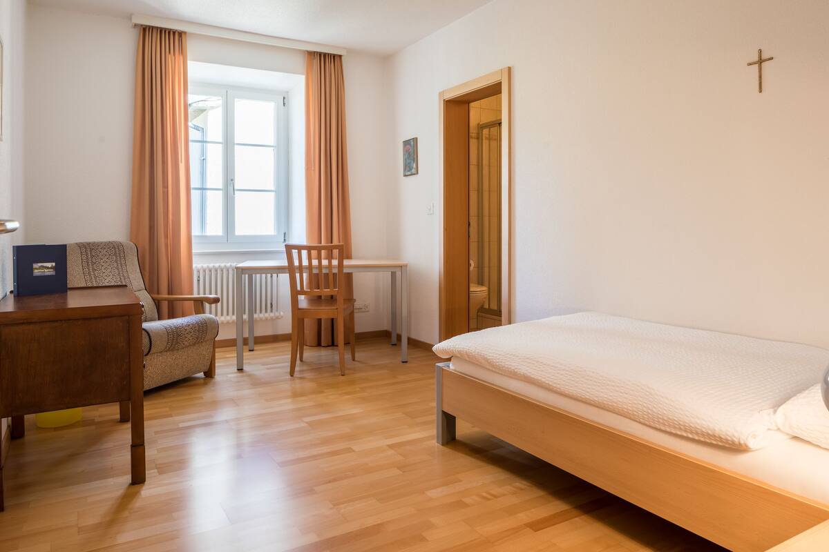 A bedroom with a wooden bed, a desk, a chair, and a window with curtains.