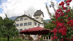 A building with a white facade, multiple windows, and a red umbrella. - Gästehaus St. Ursula (Brig)