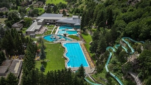 An aerial view of a resort with multiple swimming pools, a large building, and a winding water slide. - Gästehaus St. Ursula (Brig)
