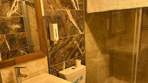 A bathroom with a marble backsplash, a sink, a toilet, and a glass shower enclosure. - Adana Akdeniz Otel (Adana)