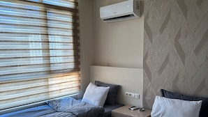 A hotel room with two beds, a window with blinds, an air conditioning unit, and a patterned wall. - Adana Akdeniz Otel (Adana)