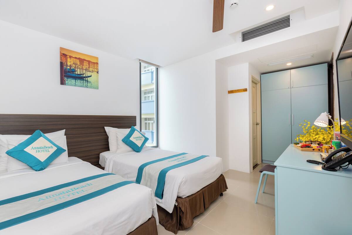 A hotel room with two beds, a desk, and a window.