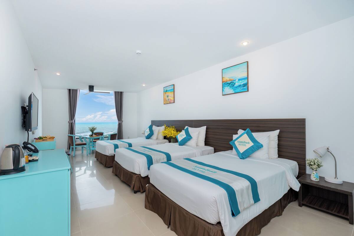 A hotel room with three beds, a desk with a telephone, a coffee maker, and a view of the sea.