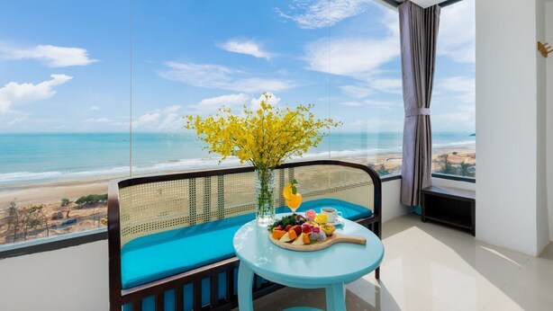 A balcony with a view of the beach, a table with a fruit platter, and a vase with yellow flowers.