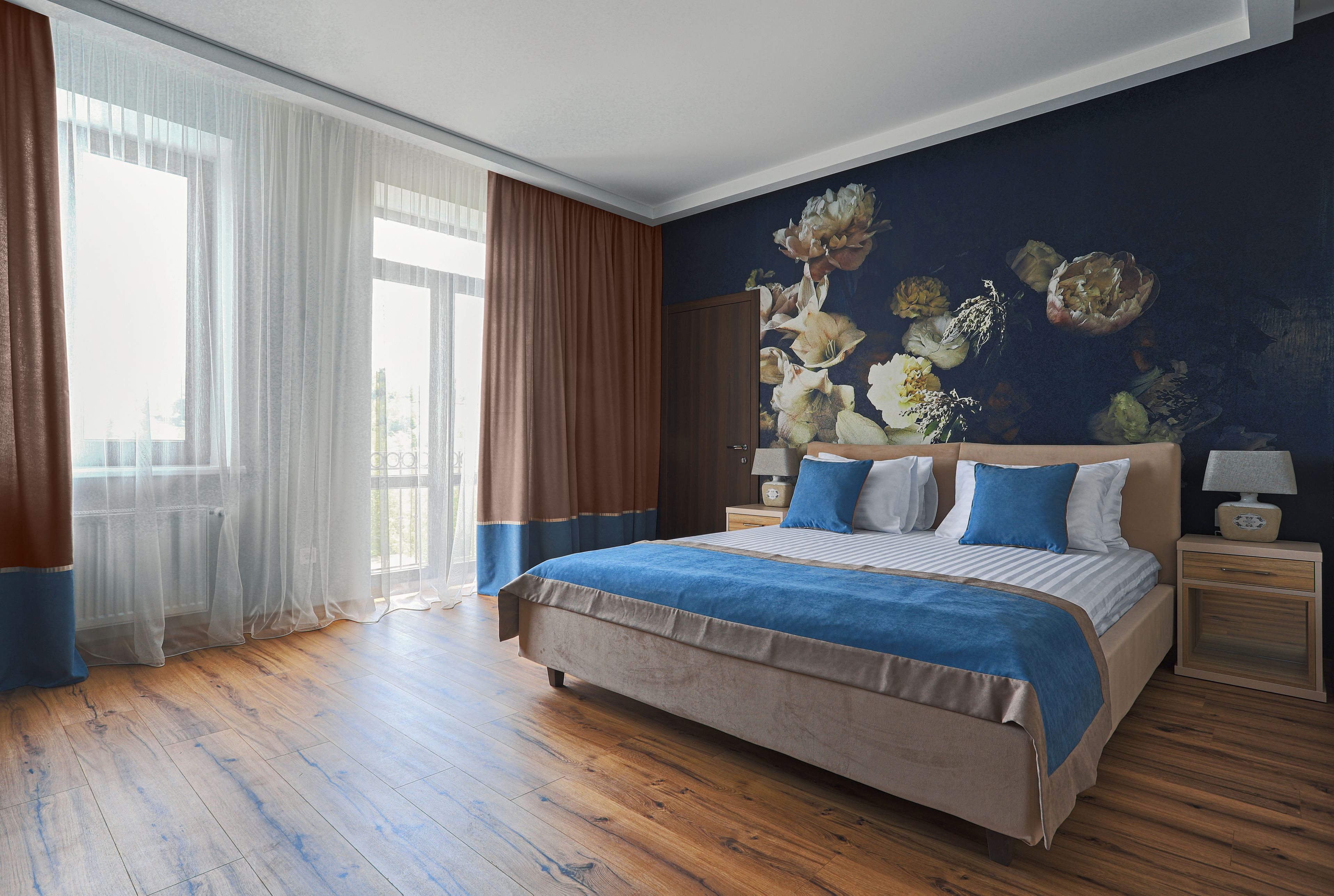 A bedroom with a large bed, a nightstand, and a wall with a floral mural.