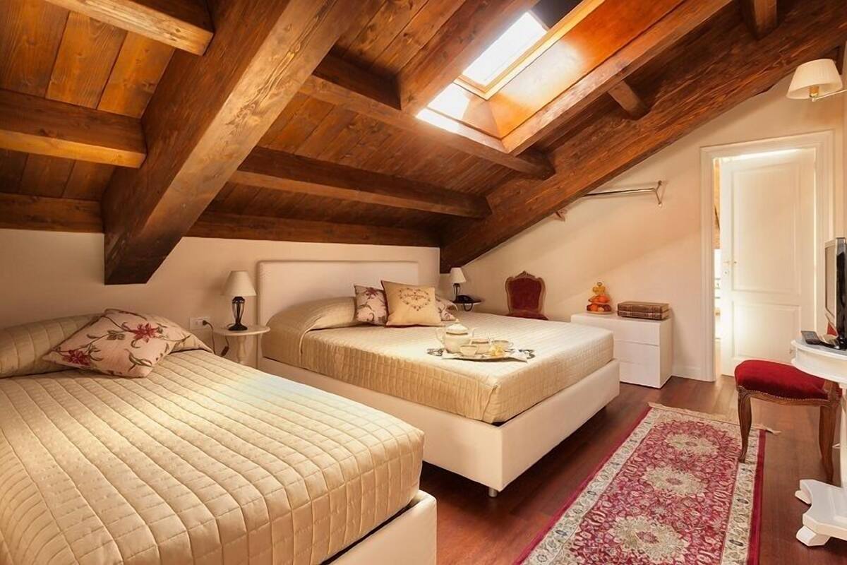 Ein gemütliches Schlafzimmer im Dachgeschoss mit zwei Betten, Holzbalken, einem Oberlicht, einem roten Teppich und einem kleinen Schreibtisch.
