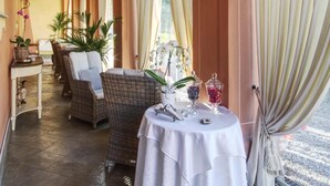 Un couloir baigné de lumière, meublé de pièces en osier, une table ronde recouverte d’une nappe blanche et de grandes rideaux.