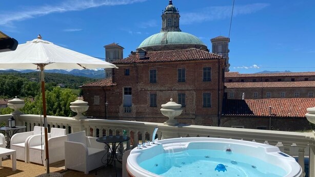Un jacuzzi sur un balcon, agrémenté de mobilier d’extérieur et d’un grand parasol, avec un bâtiment surmonté d’un dôme en arrière-plan.