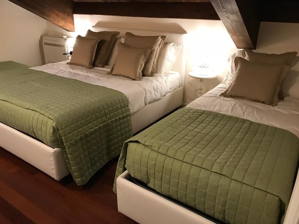 Deux lits jumeaux avec des couvertures vertes, du linge de lit blanc et une poutre en bois au plafond.