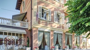 Un bâtiment à deux étages doté d’un balcon, de grandes fenêtres avec volets et de plantes en pot.