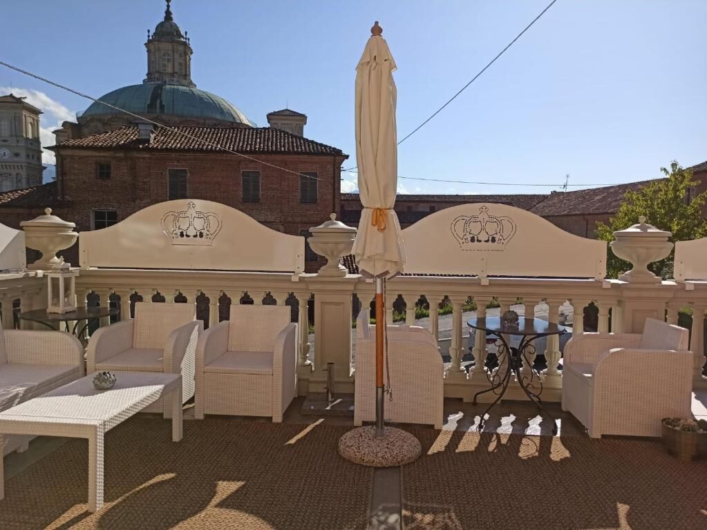 An outdoor seating area with wicker furniture, a central umbrella, and a decorative wall with a crest.