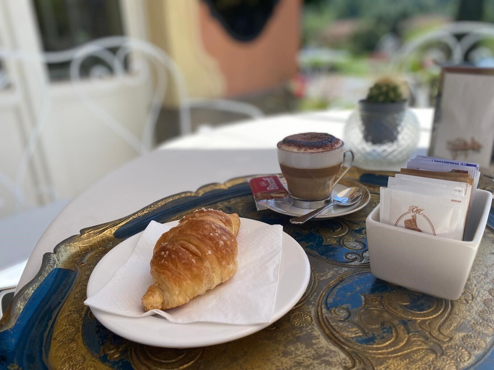 A table with a croissant, a cup of coffee, and a small plant.