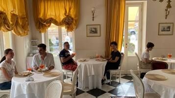 A dining area with round tables, white chairs, and yellow curtains.