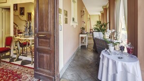 Un hall d’hôtel avec un sol à carreaux, un comptoir de réception, un espace repas avec une chaise rembourrée de couleur rouge, et une table recouverte d’une nappe blanche, ainsi que divers objets.