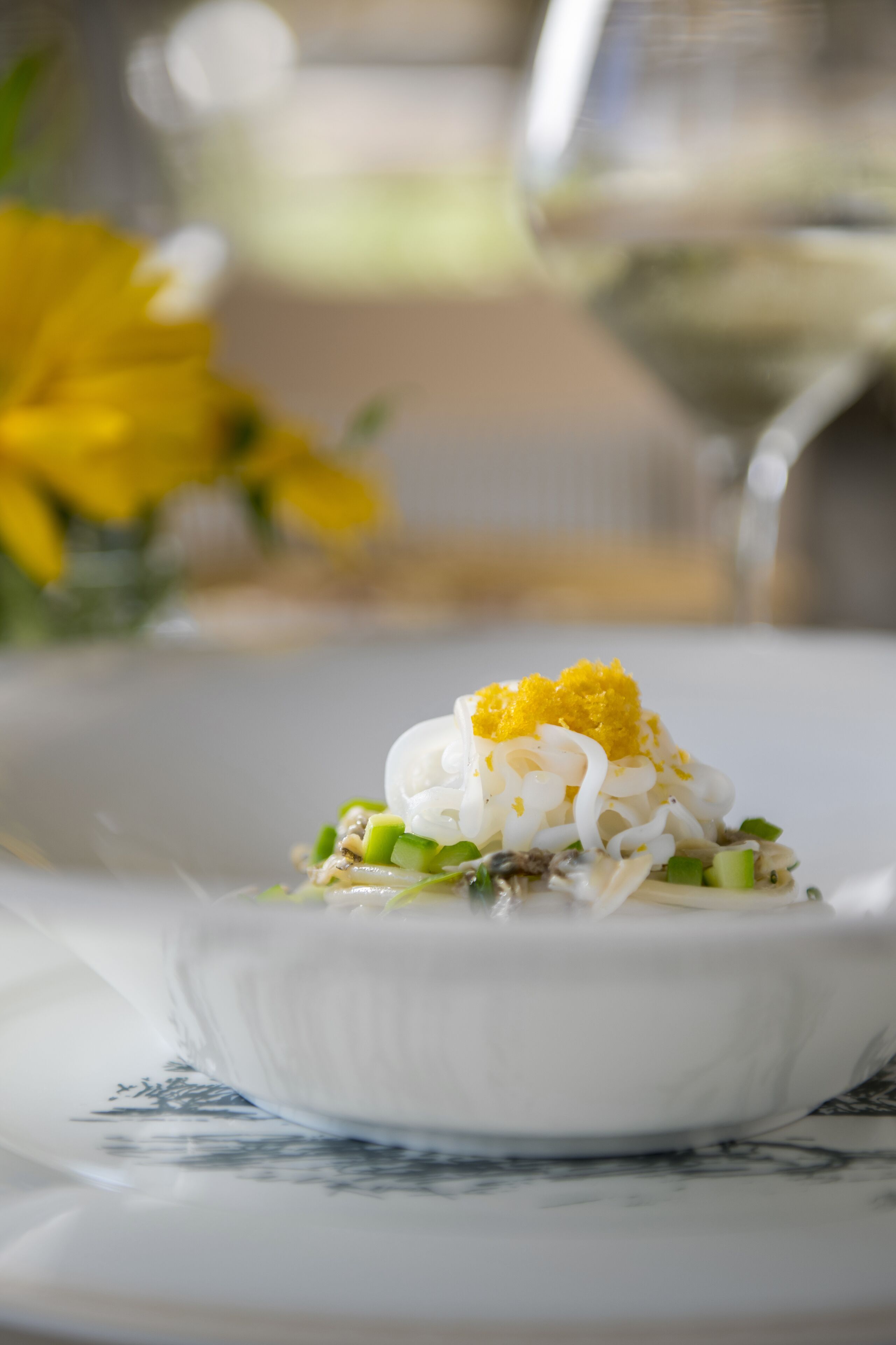 Un bol blanc contenant des nouilles, des oignons verts et une garniture jaune, le tout posé sur une table.