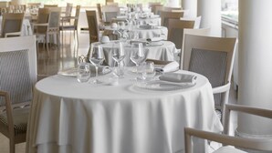 A dining area with round tables set for a meal, chairs, and a chandelier. - Residenza Parco Fellini (Rimini)