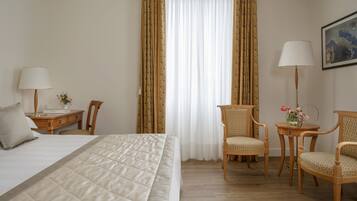 Una habitación de hotel con una cama, dos sillas, un escritorio, una lámpara y un cuadro en la pared.