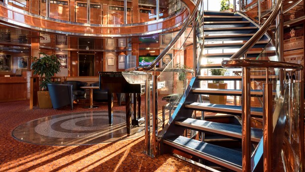 Ein großzügiger Innenhof mit einer zentralen Treppe, Sitzbereichen und einem Fernsehbildschirm.