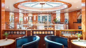 Ein luxuriöses Interieur mit einer zentralen, runden Decke, einer Sitzecke mit blauen Stühlen und einem Restaurant mit Glastüren.