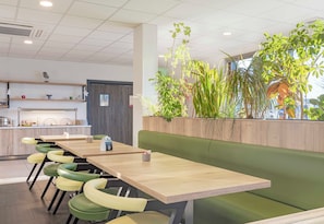 A modern dining area with wooden tables, green and yellow chairs, and a green bench.