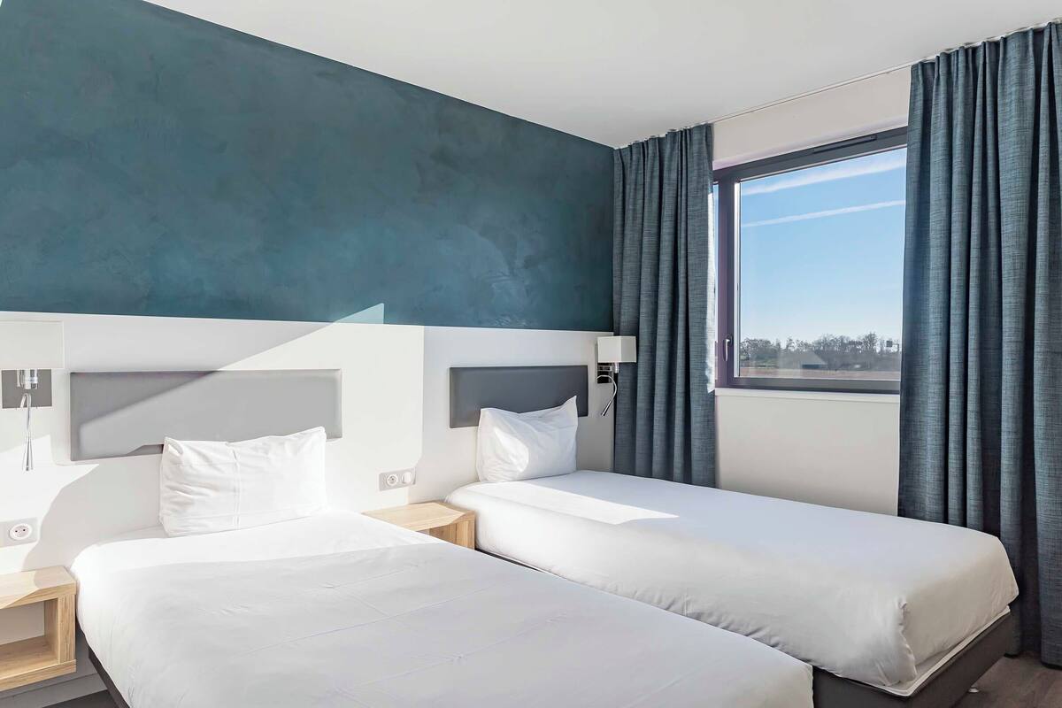 Ein Hotelzimmer mit zwei Betten, einem großen Fenster und Blick auf die Stadt.