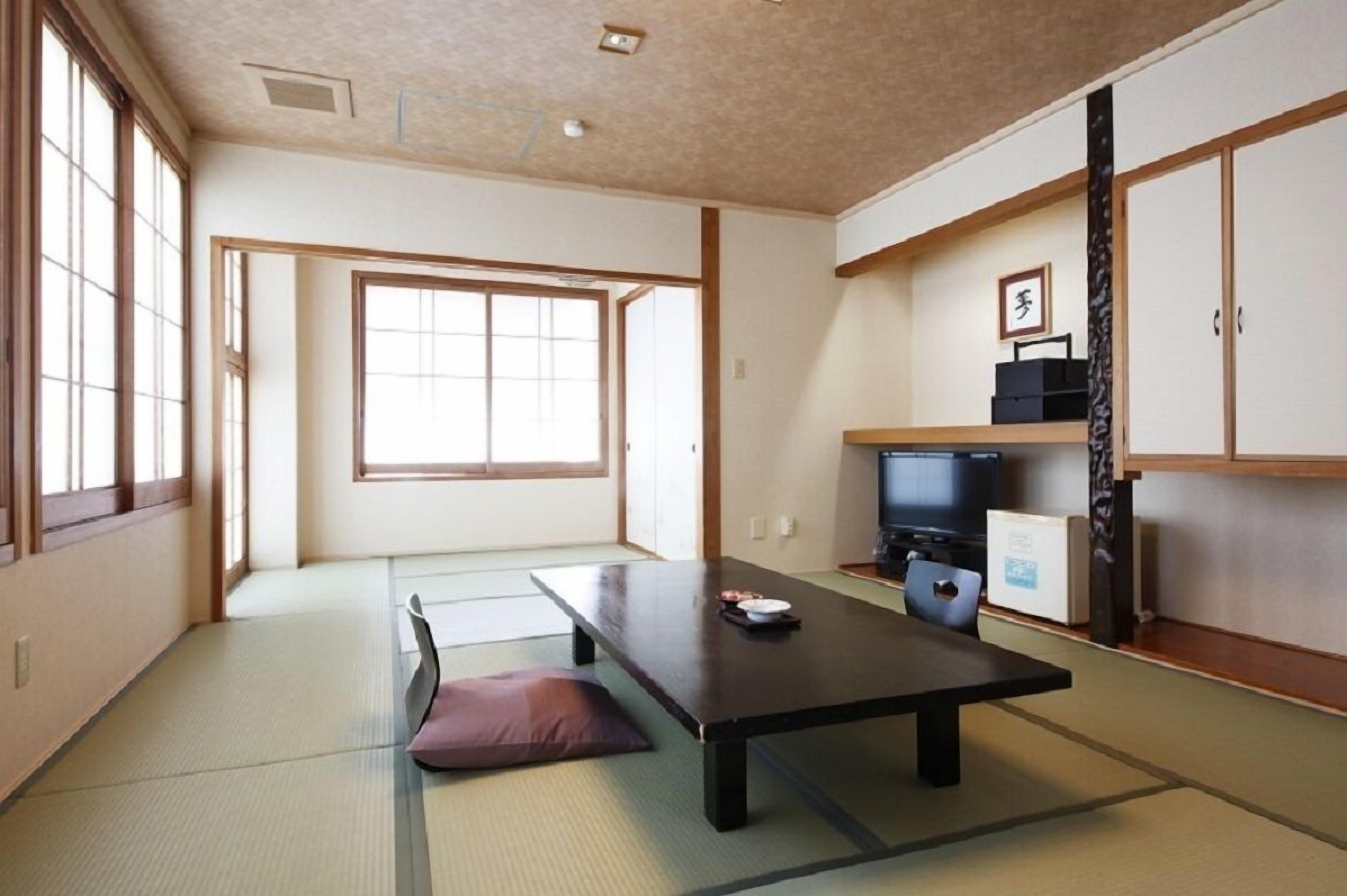 Um quarto japonês tradicional com tatames, uma mesa baixa, uma televisão e portas deslizantes.