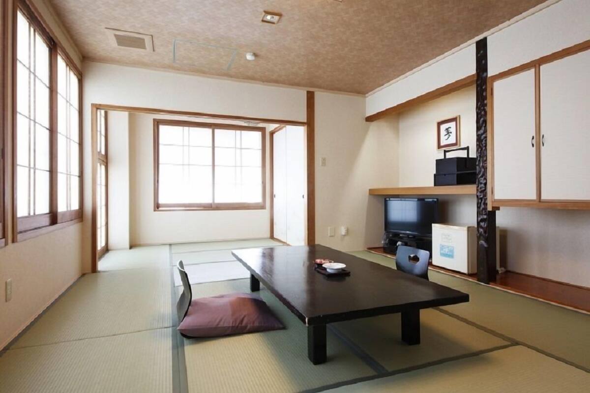 Une pièce de style japonais traditionnel, avec un sol recouvert de tatamis, une table basse, un téléviseur et des portes coulissantes.