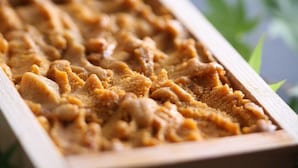 A wooden tray with a textured surface, possibly containing food or a dessert. - Koujin no Yado Sanpou (Kami)