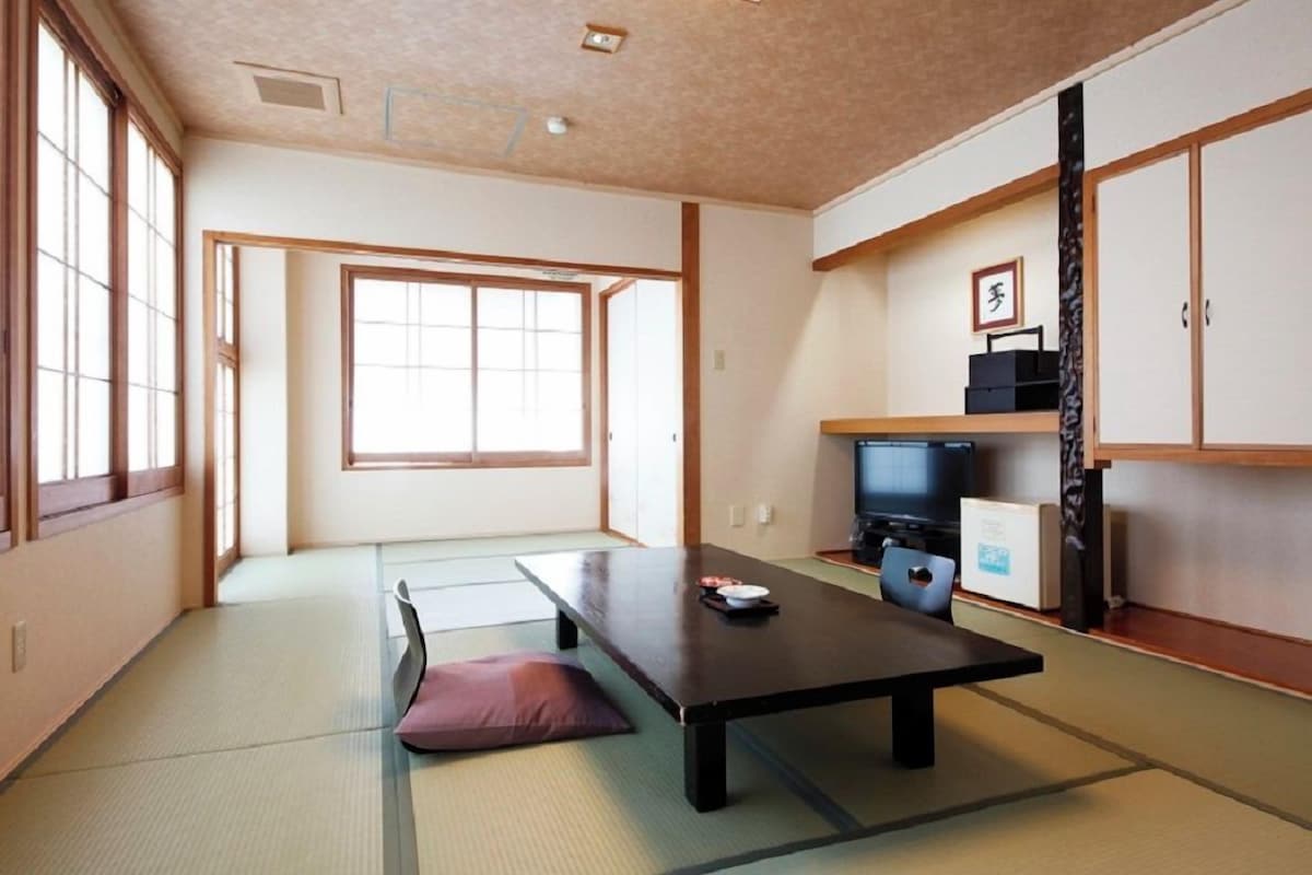 A traditional Japanese room with tatami flooring, a low table, a television, and sliding doors.