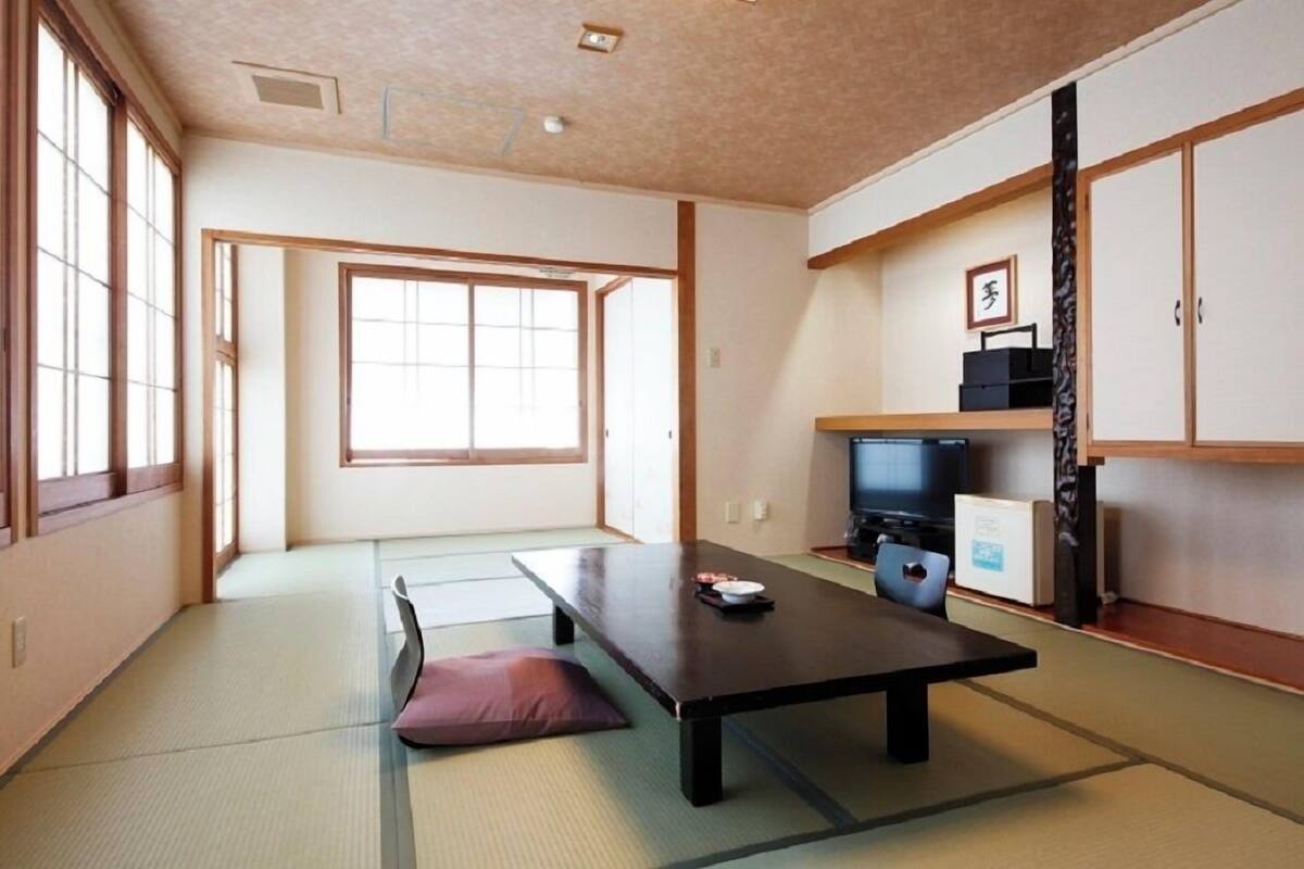 Une pièce de style japonais traditionnel, avec un sol recouvert de tatamis, une table basse, un téléviseur et des portes coulissantes.