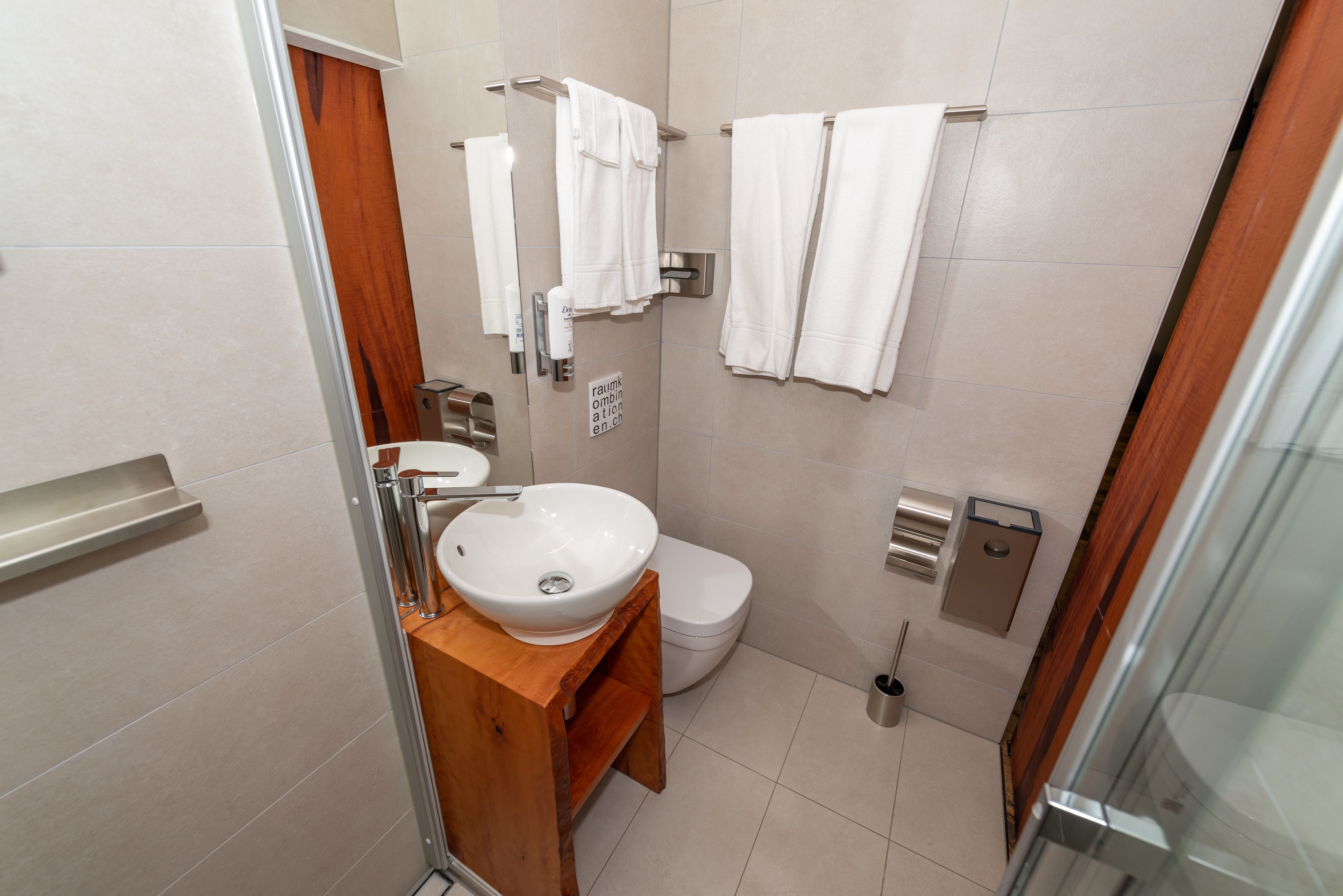 Une salle de bain moderne avec un meuble-lavabo en bois, un lavabo blanc, des toilettes et une douche à parois de verre.