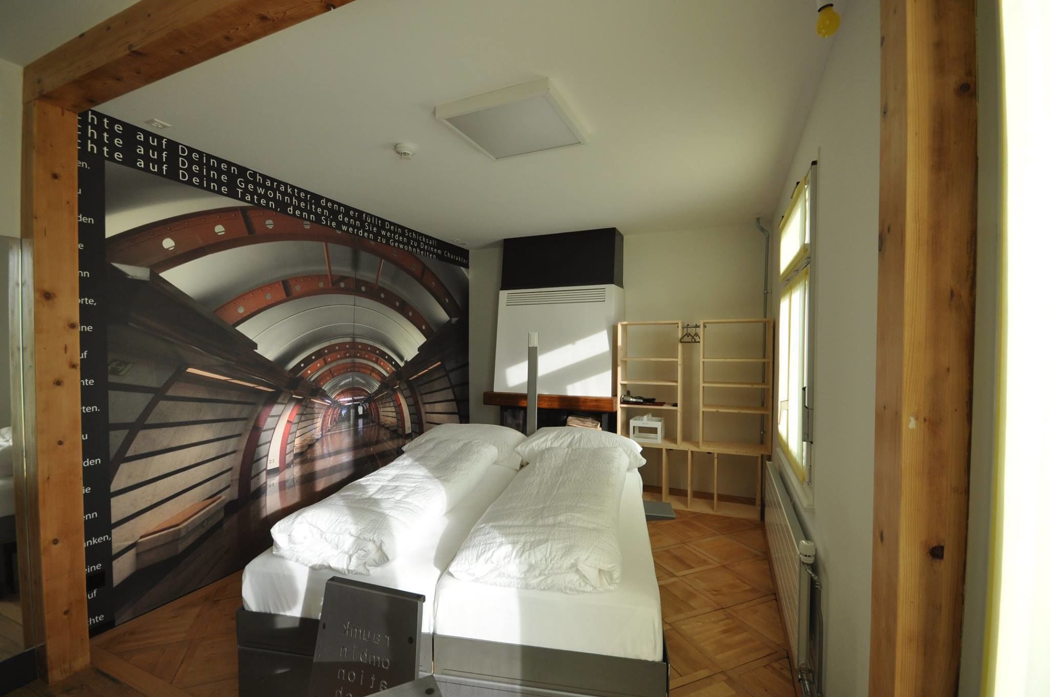 Quarto com cama, radiador, prateleira e parede com desenho circular.